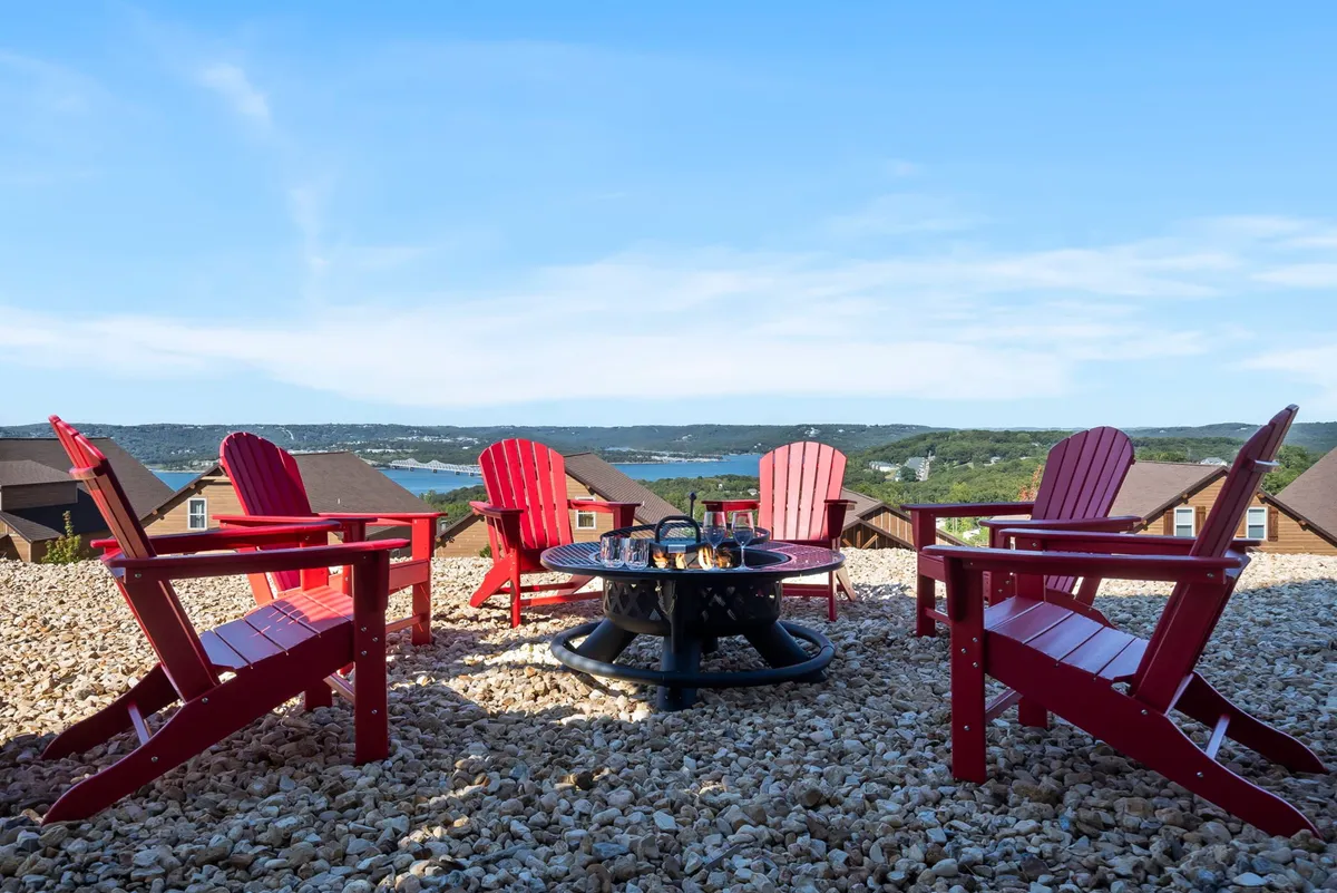 Red Adirondack chairs circle a fire pit overlooking the lake, with a clear view of the water and fading sunset colors. The relaxed outdoor setup suggests a space for gathering, unwinding, and enjoying the scenery just steps from the shoreline.