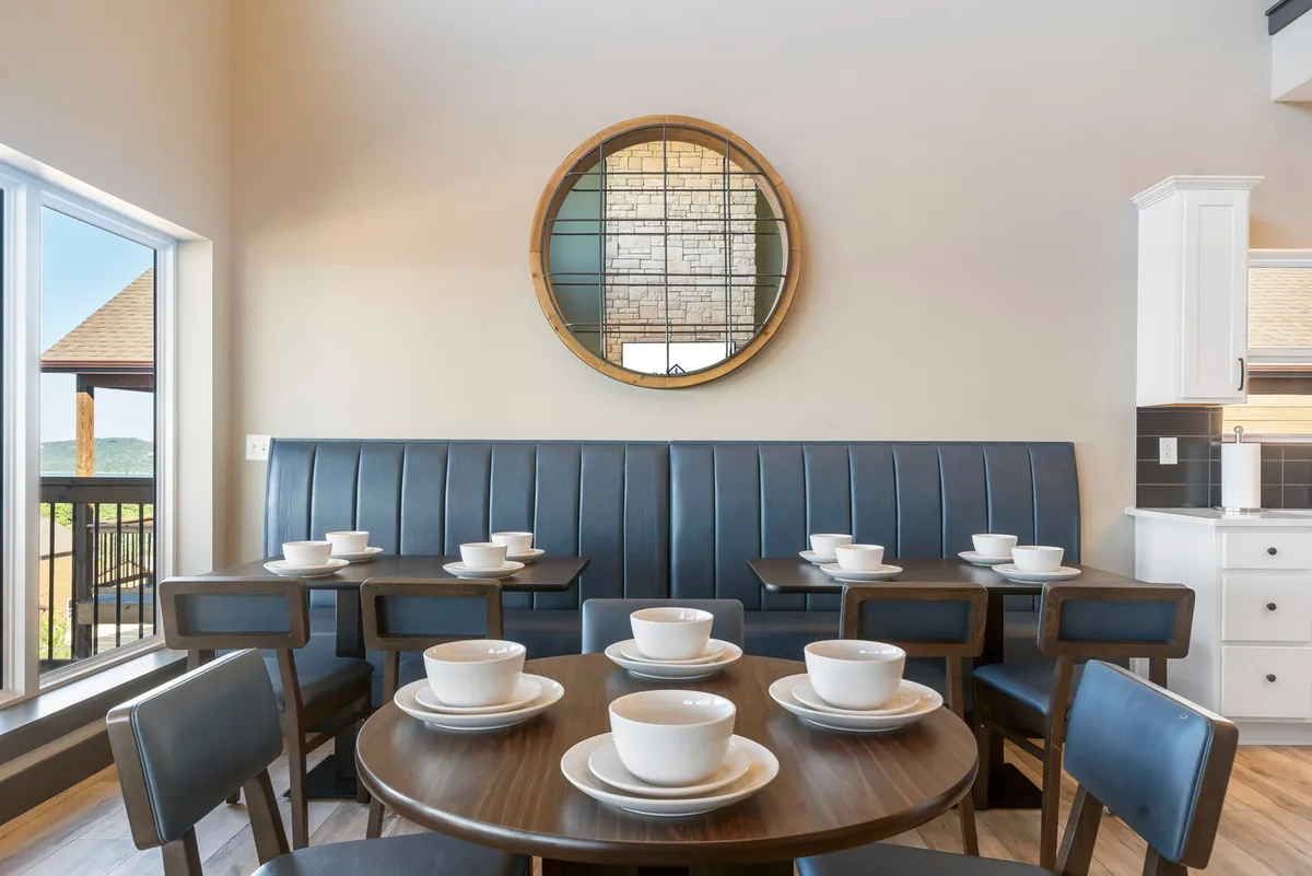 A welcoming loft area featuring a round wooden table and blue leather seating set beside a decorative mirror. The space offers a cozy nook for morning coffee or intimate conversations, with soft light and thoughtful decor.