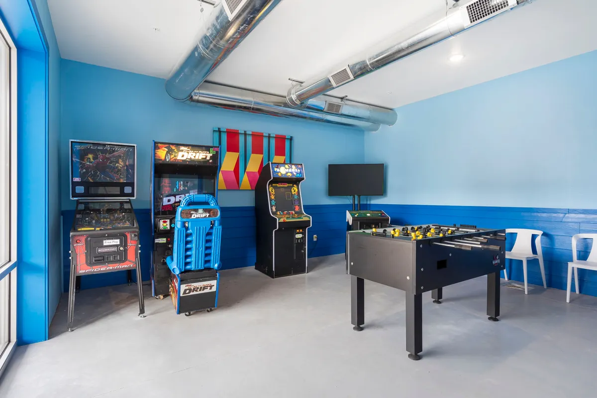 A dynamic view of another game room setting, showcasing arcade machines, a foosball table, and colorful decor. The room is bustling with activity potential, providing ample space for tournaments, retro game sessions, and group interactions.