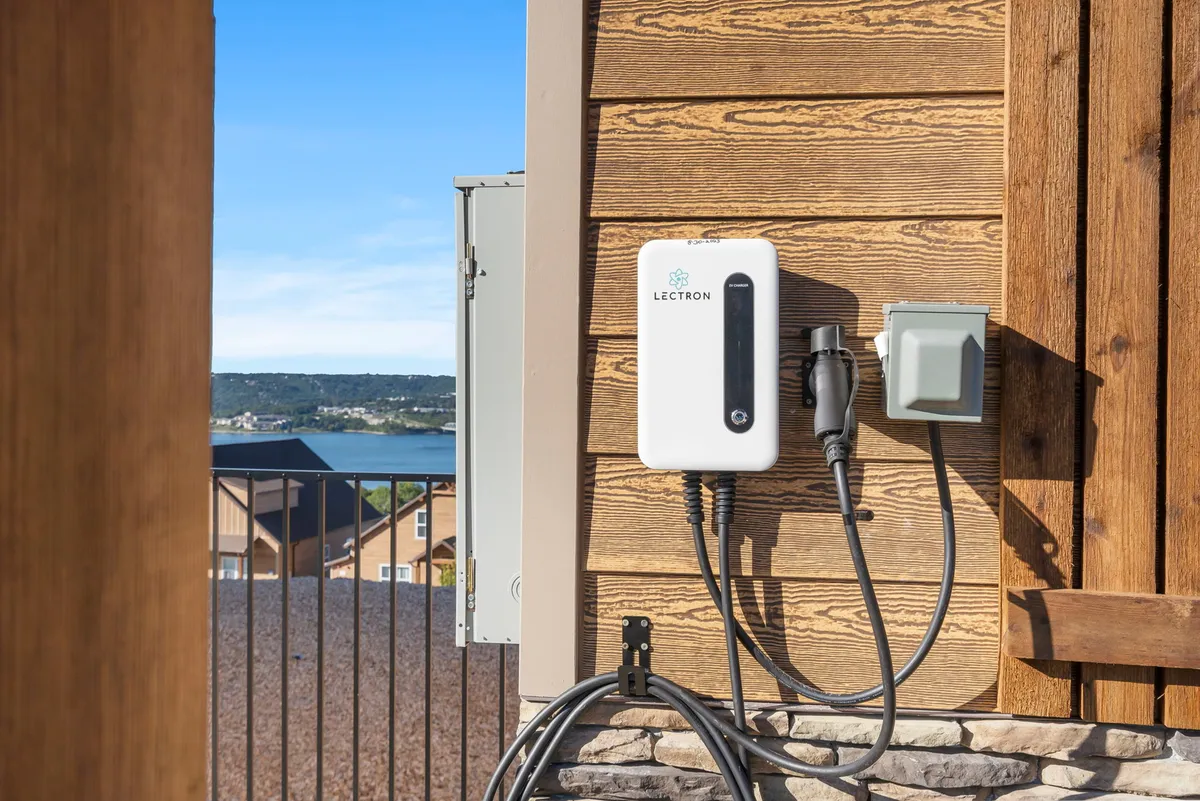 A modern exterior shot featuring an electric vehicle charger mounted on the wooden siding of the home, set against a landscaped view. The scene feels contemporary and eco-friendly, implying a commitment to modern conveniences for guests.