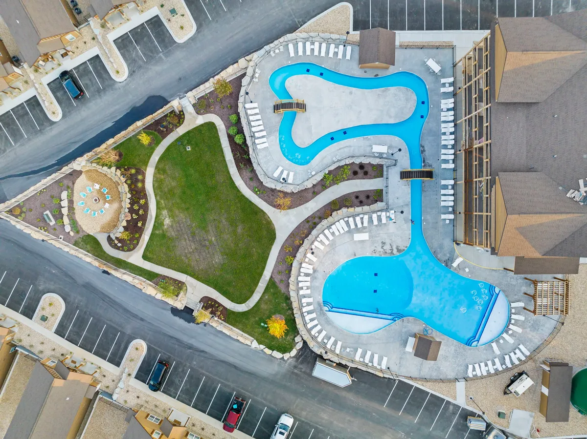 An exterior view of several swimming pools surrounded by a well-kept green lawn, comfortable seating areas, and adjacent resort buildings. The pools are framed by sunset lighting, creating an inviting and social atmosphere.