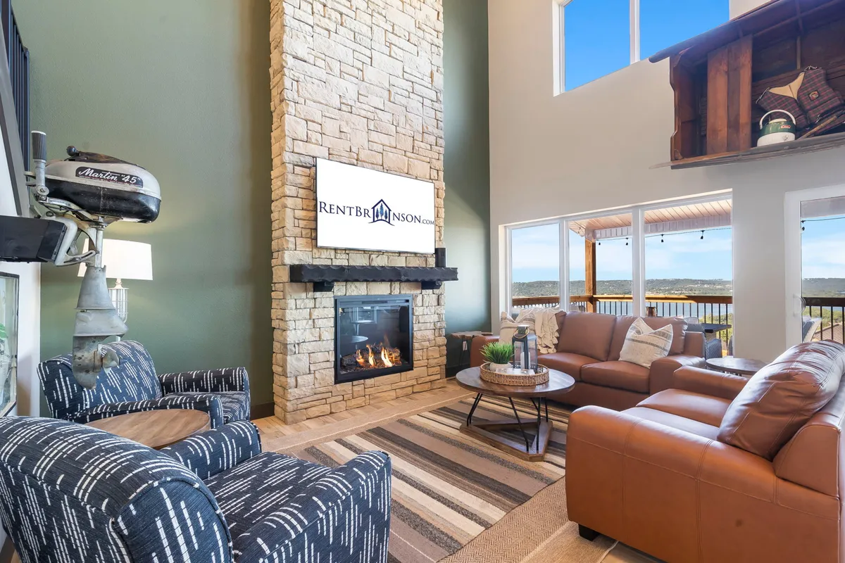 A cozy living area with a prominent stone fireplace, comfortable seating, and large windows framing the scenic outdoors. The decor is modern yet warm, inviting guests to relax or gather for social activities with a beautiful view.