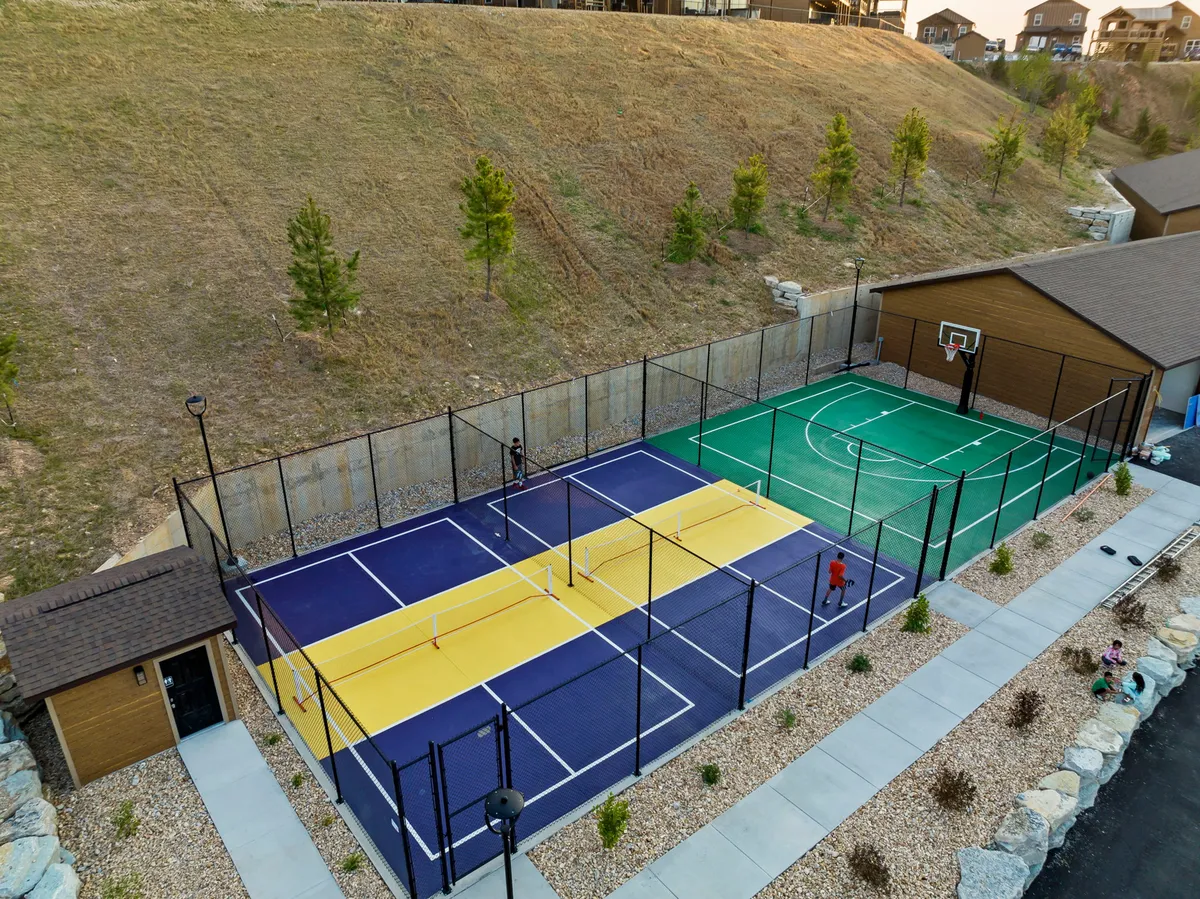 A vibrant exterior space featuring tennis and basketball courts surrounded by lush greenery, with families actively playing and engaging in outdoor games. The scene is energetic and communal, suggesting a lively environment for group activities.