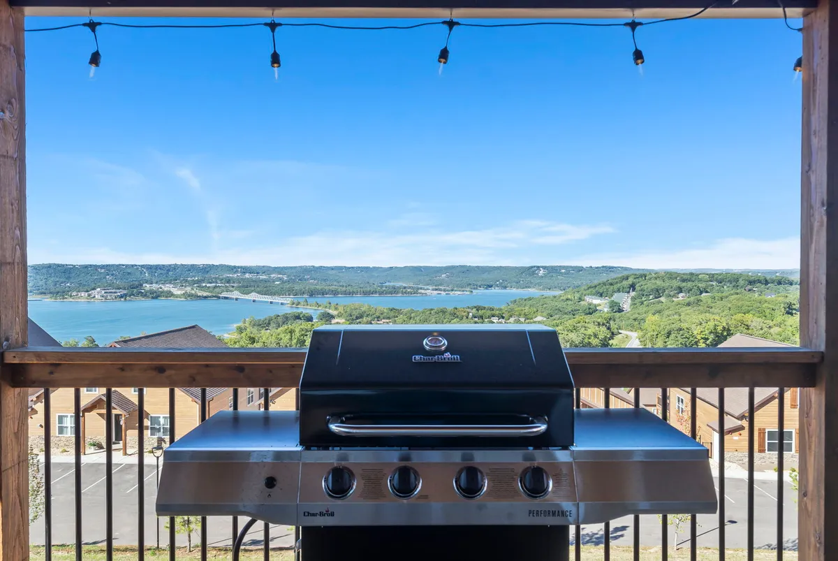 An exterior deck with a grill and scenic views of the lake and hills. The space is set up for outdoor dining or sunset toasts, inviting guests to transition seamlessly from indoors to outdoors for socializing and relaxation.